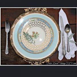 Vintage table setting with blue-and-gold plates, fork, knife, spoon, and napkin on a dark wooden table