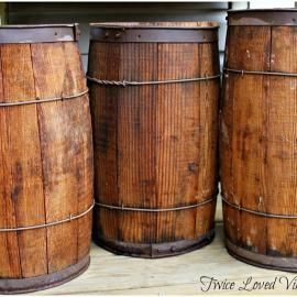 Three wooden barrels with metal bands, standing side by side on a shelf.