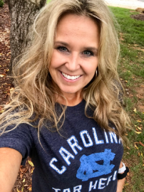 Smiling woman in a navy Carolina Panthers T-shirt outdoors by a tree.