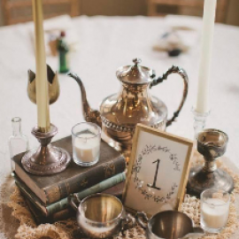 Tea set on a table with brass teapot, candles, glasses, and a “1” card in a cozy setting