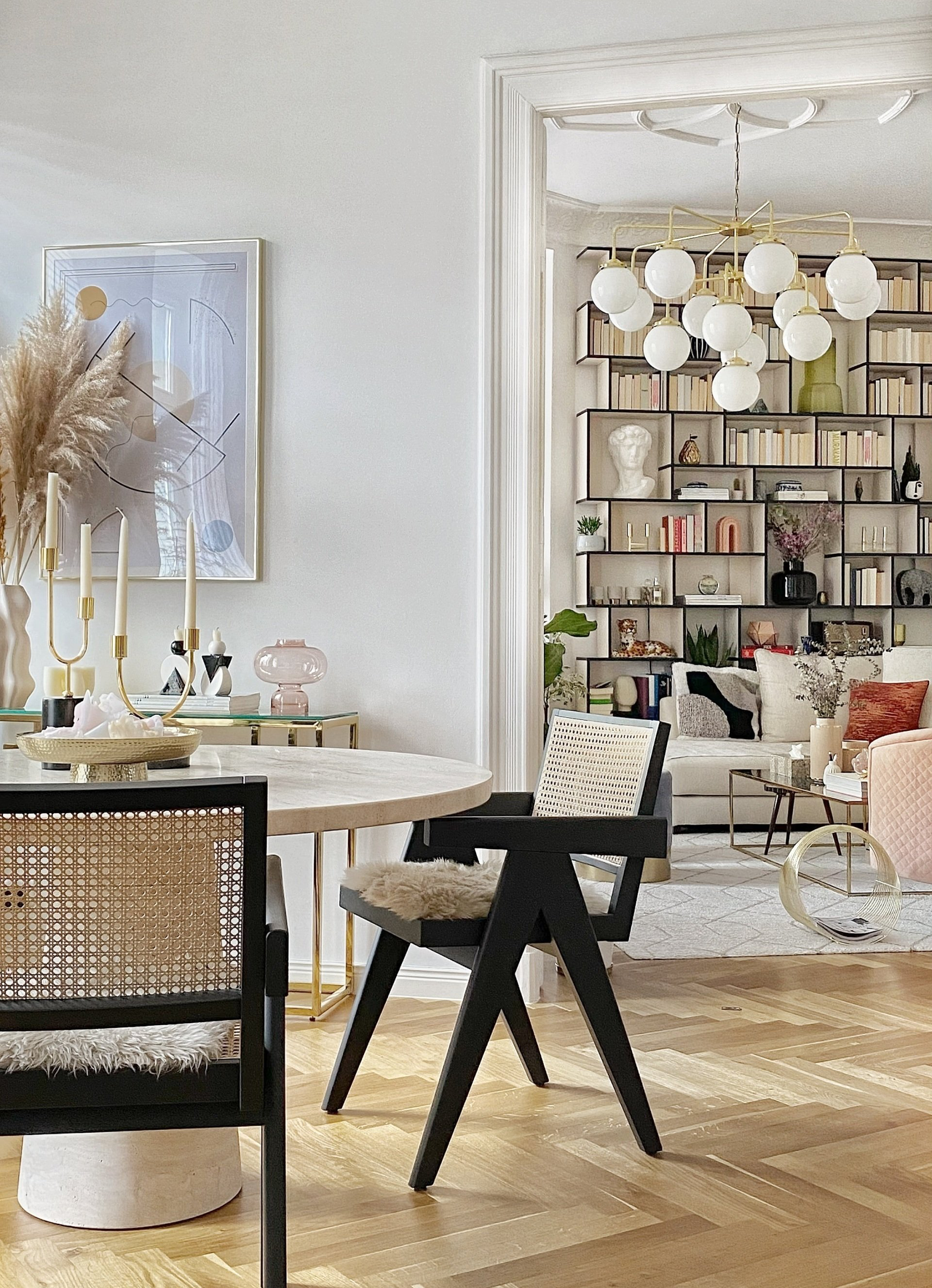 Dining room with modern chairs, round table, open doorway to a living room with bookshelves.