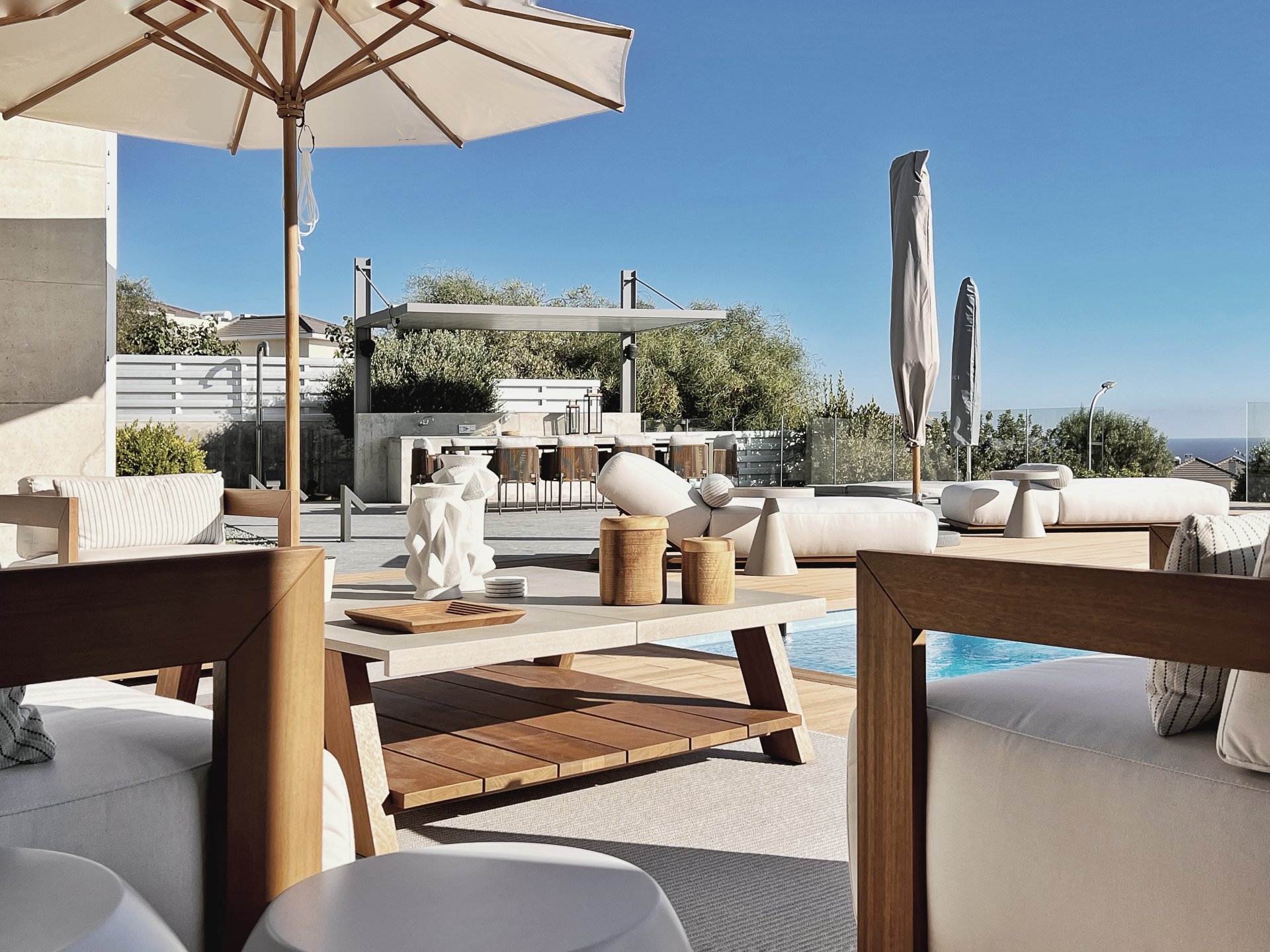Patio with pool: white furniture, sun umbrella, blue sky.