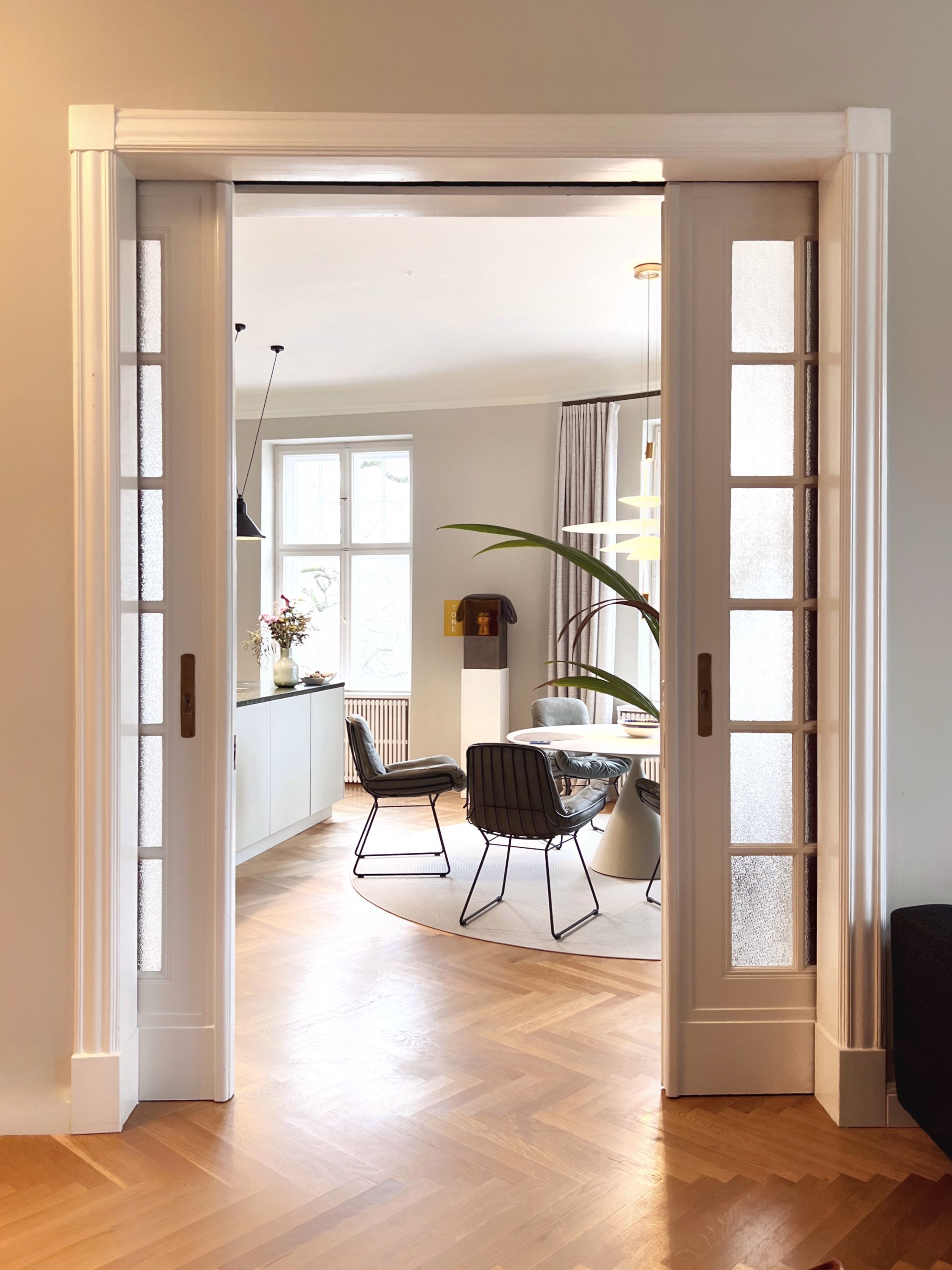 Open, white-framed pocket doors reveal a dining room with a round table and chairs; wooden floors throughout.