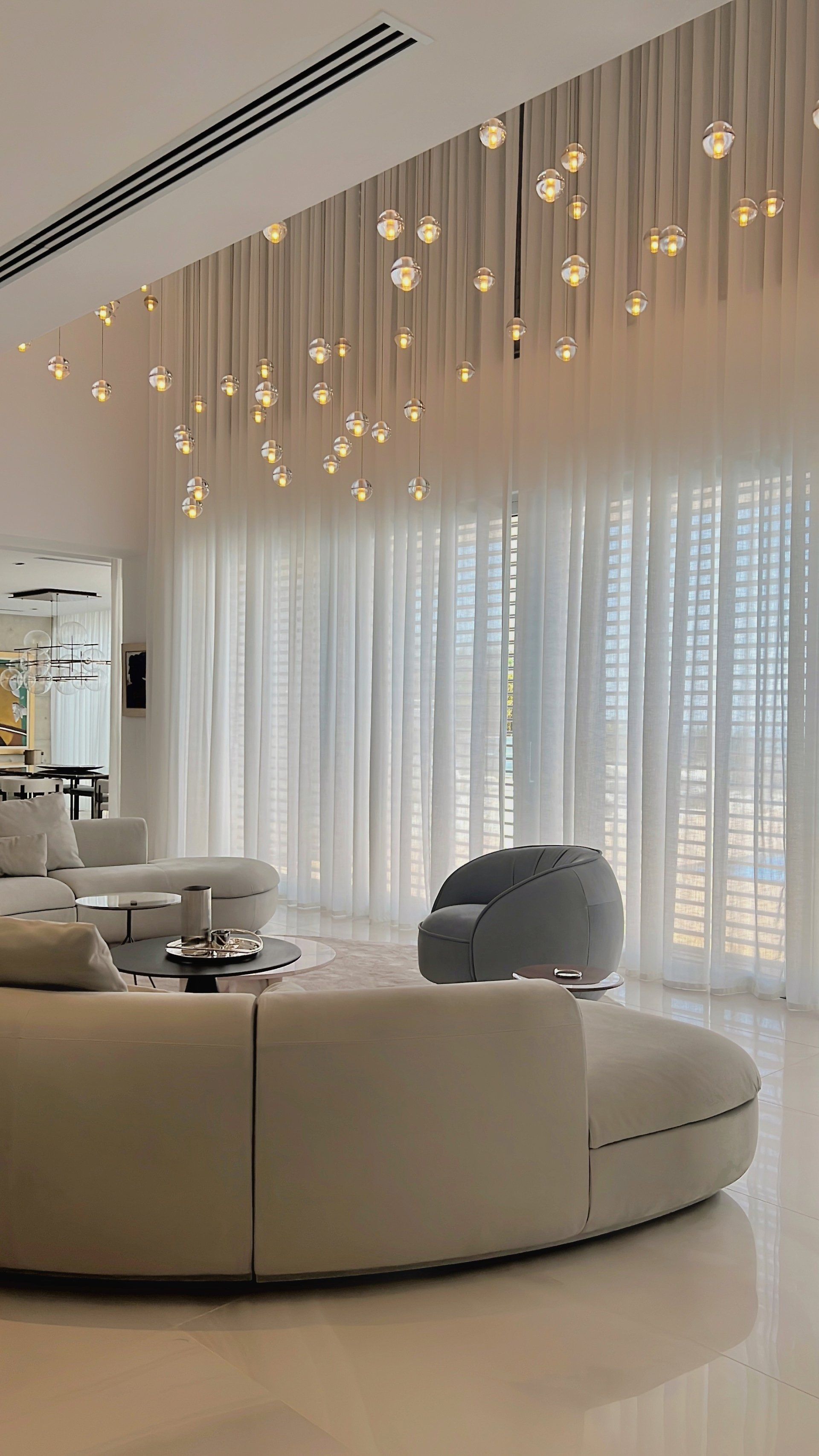 Beige living room with curved sofa, sheer curtains and pendant lights