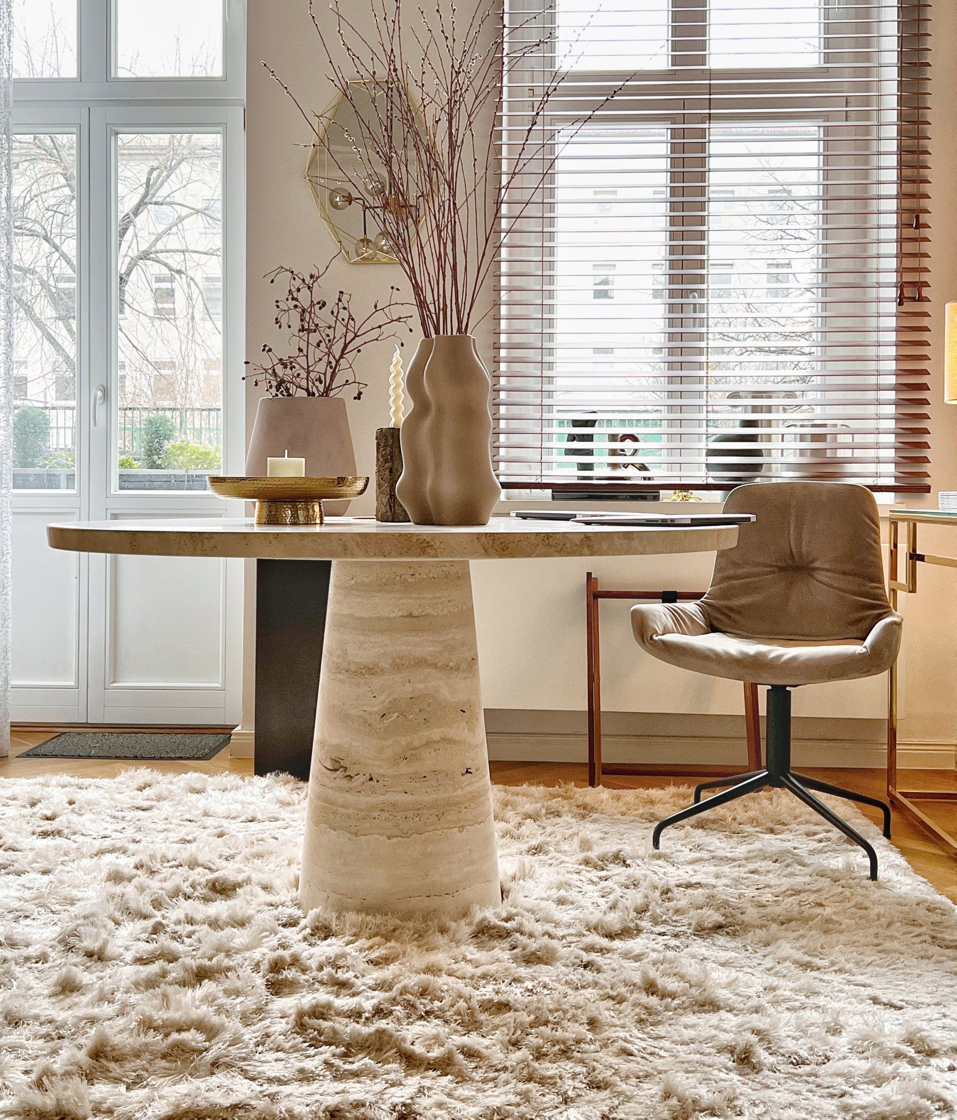 Beige dining table, stone base, neutral rug, window, chair.
