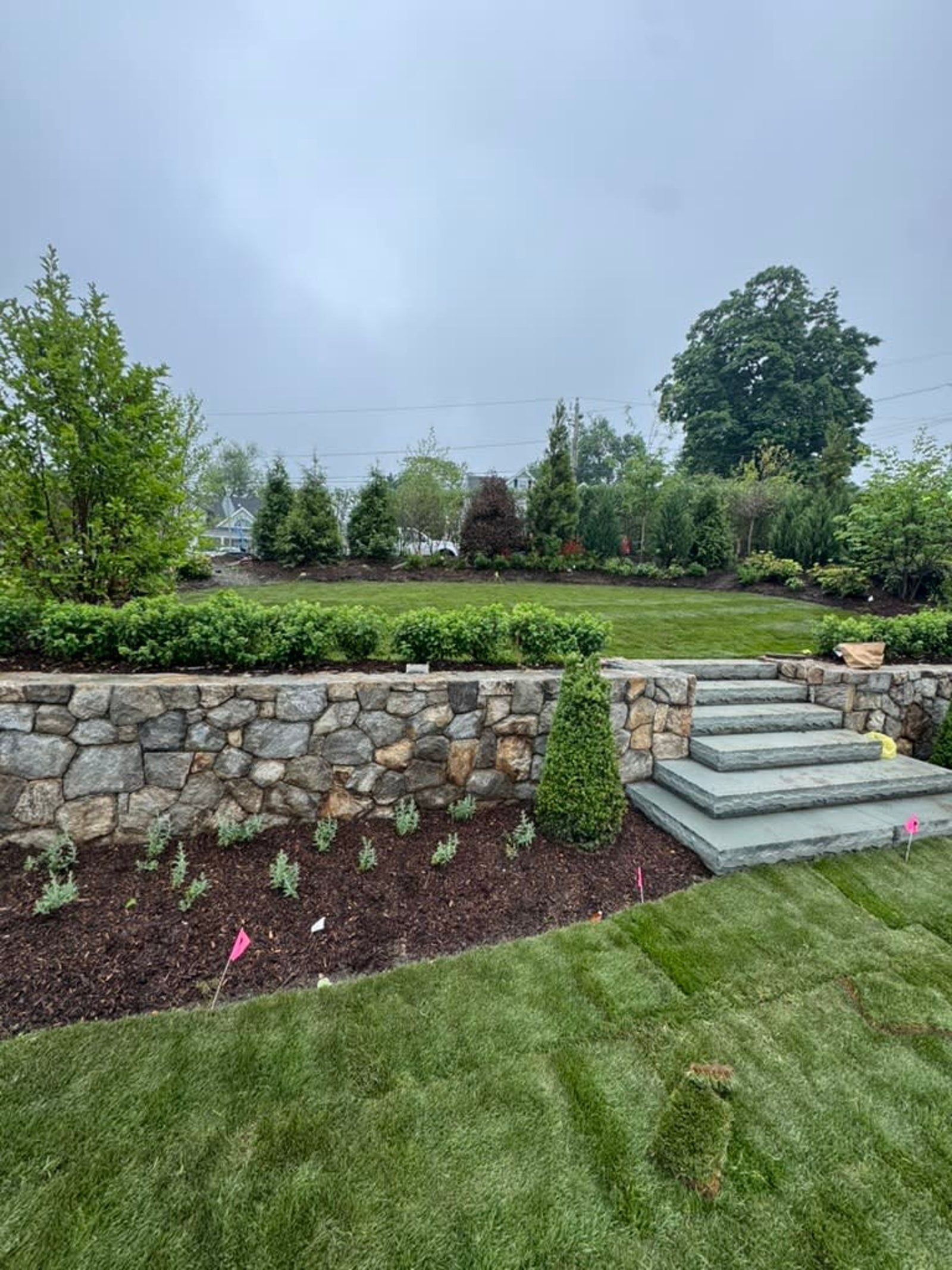 Stone garden wall and steps beside a manicured lawn and landscaped shrubs on an overcast day