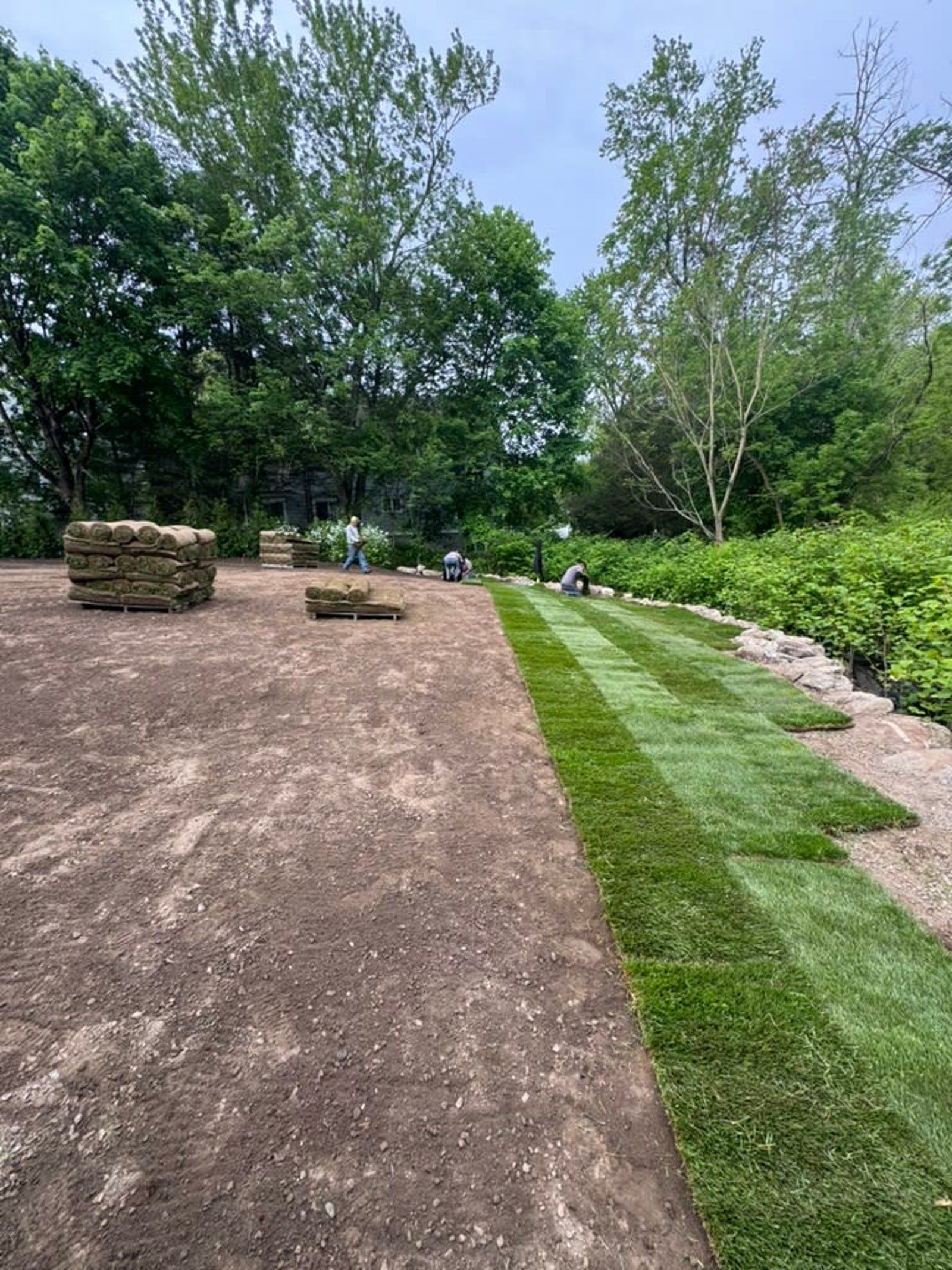 Gravel path beside a mowed green lawn, with stacked stones and trees in a wooded landscape