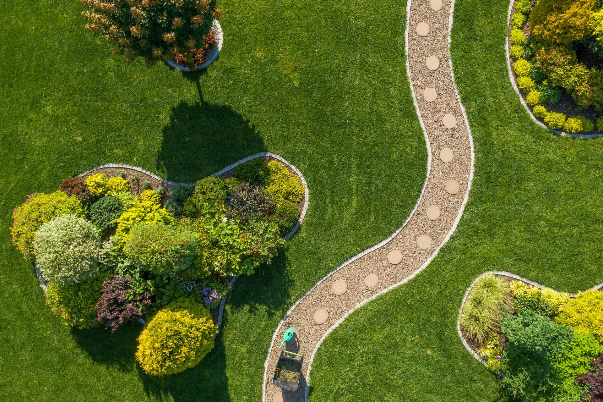 Aerial view of a winding stone path through a green garden with shrubs and trees.