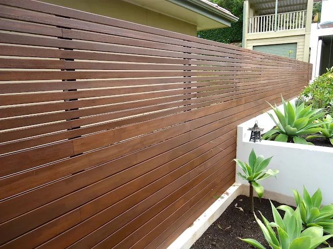 A Wooden Fence Surrounds A Lush Green Lawn In Front Of A House — Ballina Best Fencing In Ballina, NSW