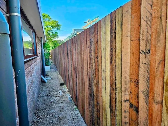 A Wooden Fence Is Surrounded By White Pillars And Bushes — Ballina Best Fencing In Ballina, NSW