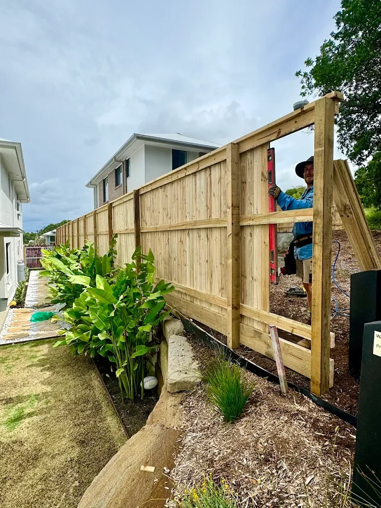 A Close Up Of A Wooden Fence half built with a guy holding up a level— Ballina Best Fencing In Ballina, NSW