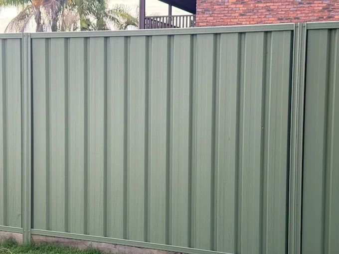 A Long Red Metal Fence Along A Cobblestone Street — Ballina Best Fencing In Ballina, NSW
