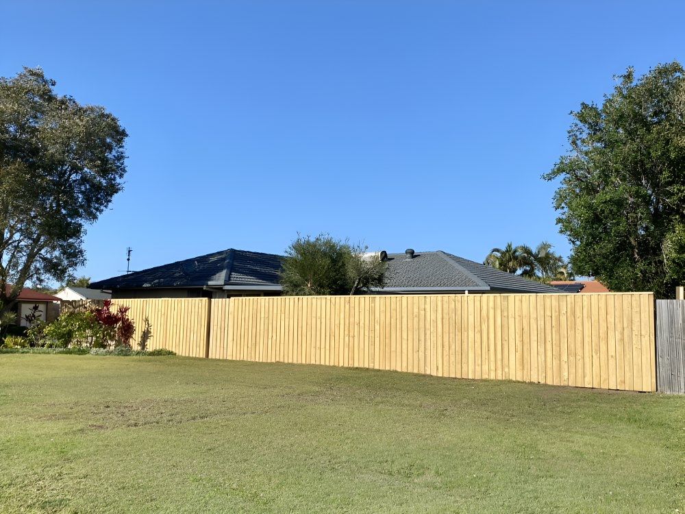 A Wooden Fence Surrounds A Grassy Field In Front Of A House — Ballina Best Fencing In Ballina, NSW