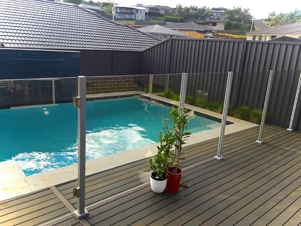 A Swimming Pool Is Surrounded By A Glass Fence And A Wooden Deck — Ballina Best Fencing In Ballina, NSW