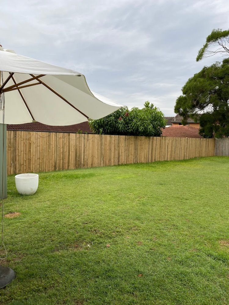 A White Umbrella Is Sitting In The Middle Of A Lush Green Yard — Ballina Best Fencing In Ballina, NSW