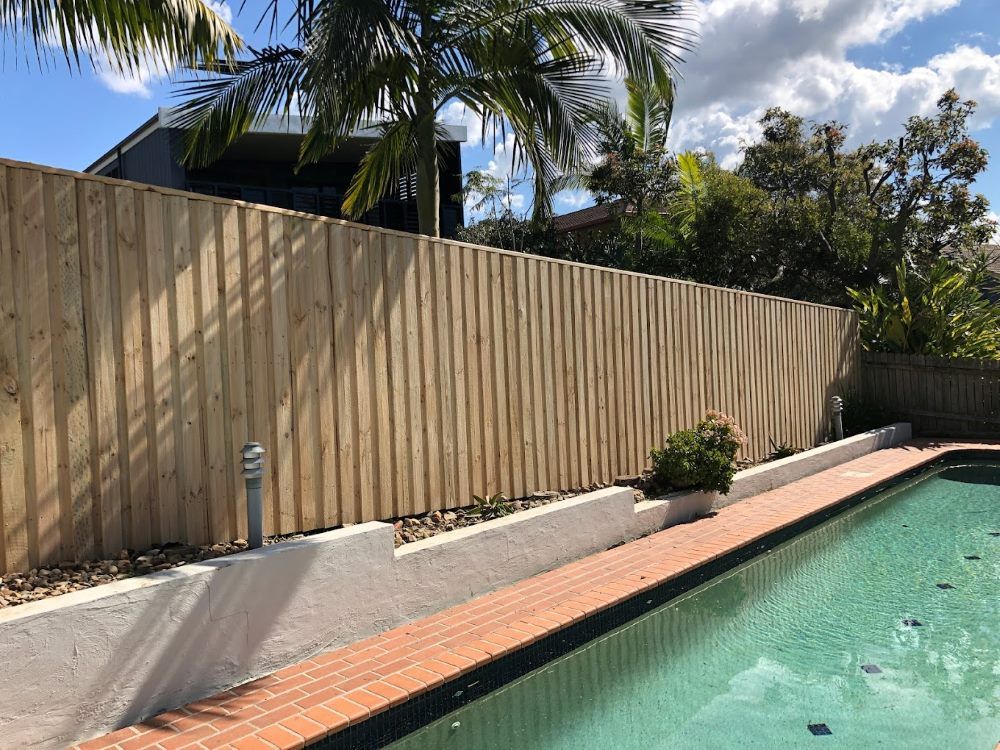A Wooden Fence Surrounds A Swimming Pool In A Backyard — Ballina Best Fencing In Ballina, NSW