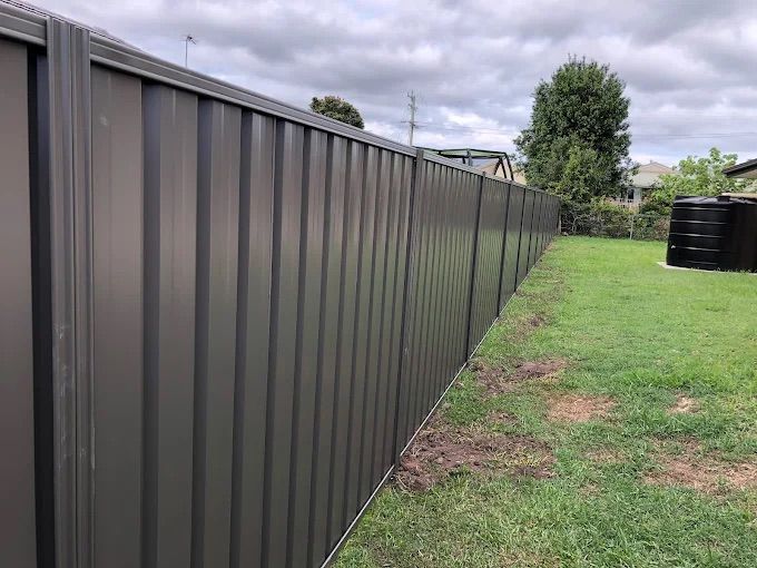 A Gray Fence Is Sitting In Front Of A House — Ballina Best Fencing In Ballina, NSW