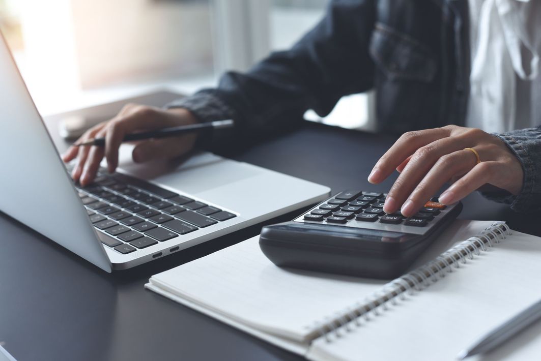 Person using a laptop and calculator with a notebook.