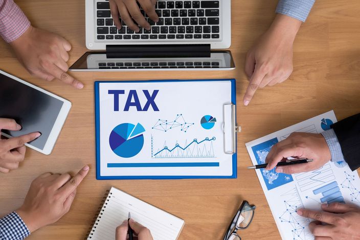 People at a table review tax documents and charts, with a laptop and tablet present.