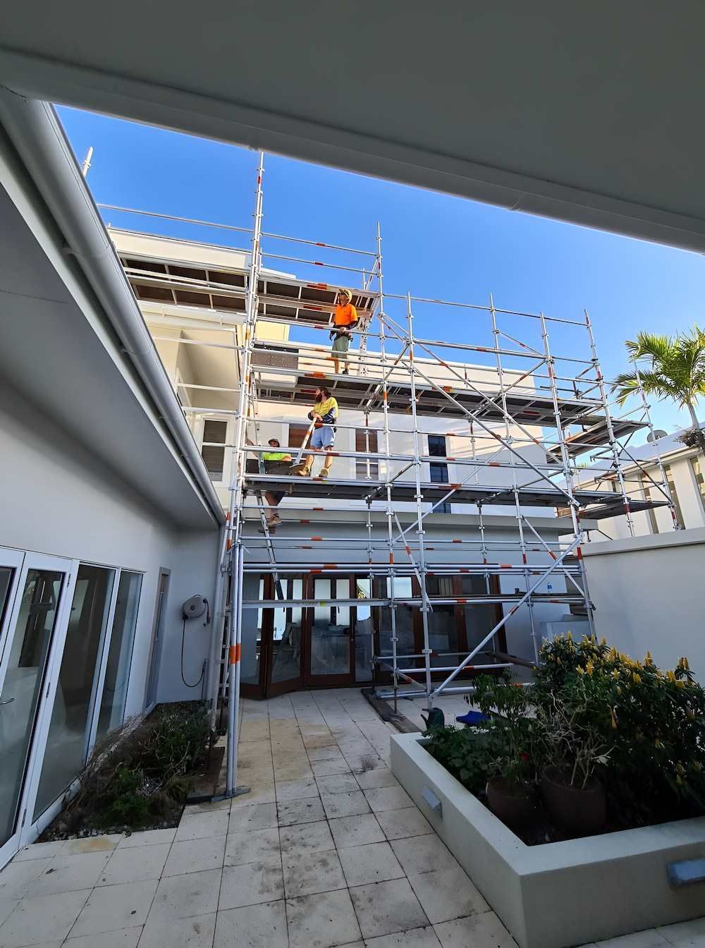 A Man is Standing on a Scaffolding on the Side of a Building — All Coast Scaffolding In Maroochydore, QLD