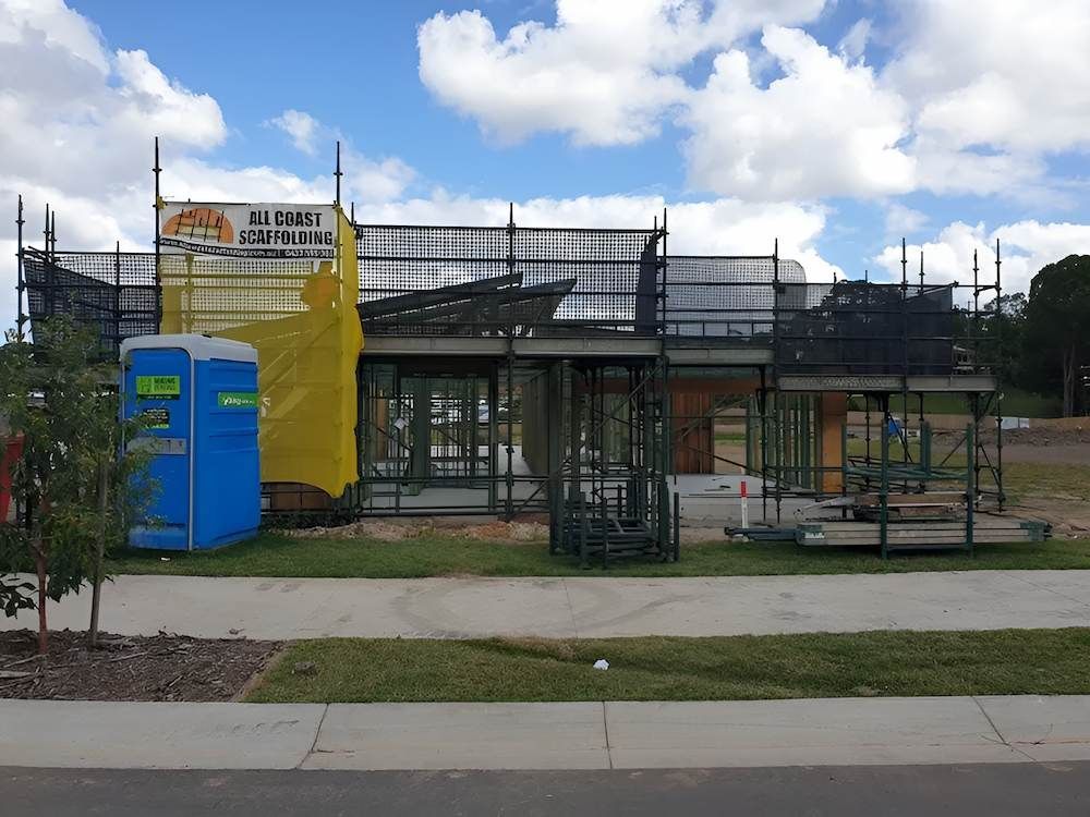 A Blue Portable Toilet is Sitting in Front of a Building Under Construction — All Coast Scaffolding In Yandina, QLD