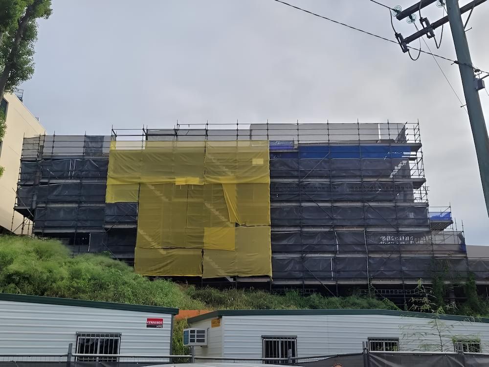 A Large Building is Covered in Scaffolding and a Yellow Tarp — All Coast Scaffolding In Yandina, QLD