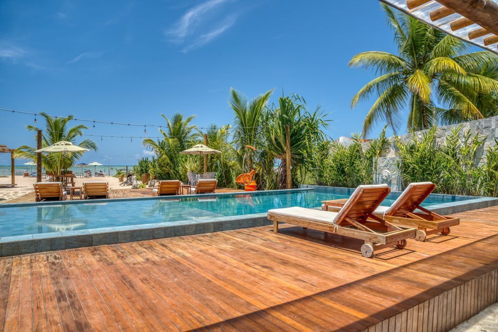 Cena à beira da piscina com deck de madeira, espreguiçadeiras e vista para o mar sob um céu azul.Pousada Villa Italiana
