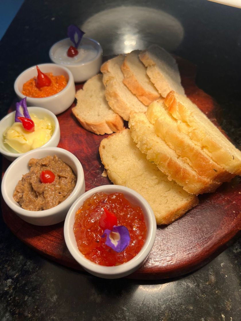 Fatias de pão com vários molhos, incluindo branco, laranja e integral, sobre uma tábua de madeira.Pousada Villa Italiana