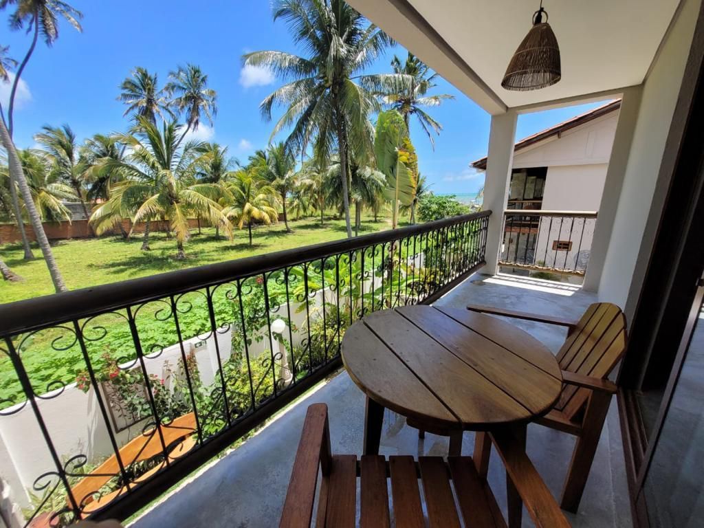 Varanda com mesa e cadeiras de madeira com vista para o gramado verde e palmeiras sob um céu azul.Pousada Villa Italiana