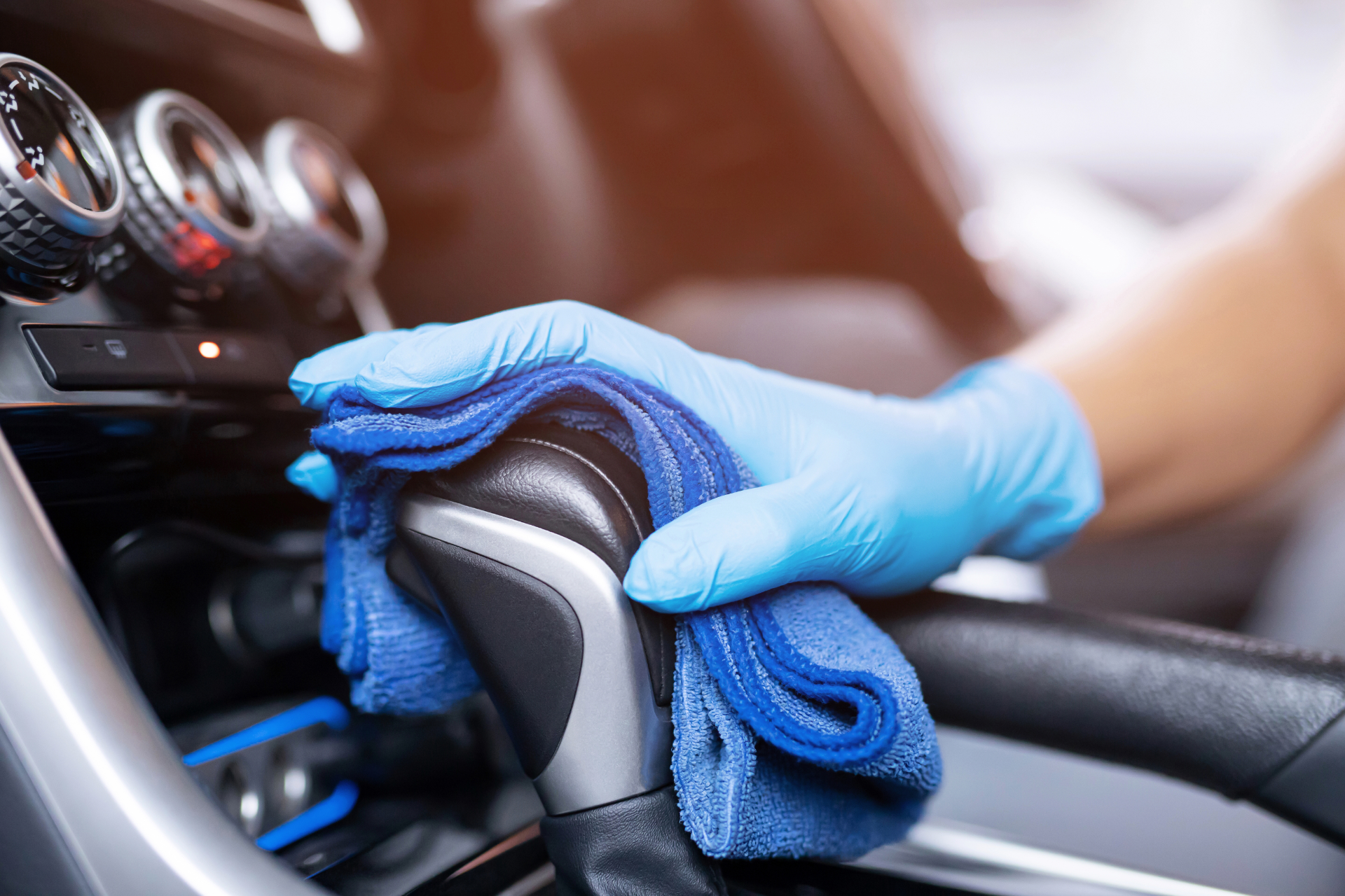 Person wiping a car's windshield with a blue cloth. Sunlight reflects off the dark car.