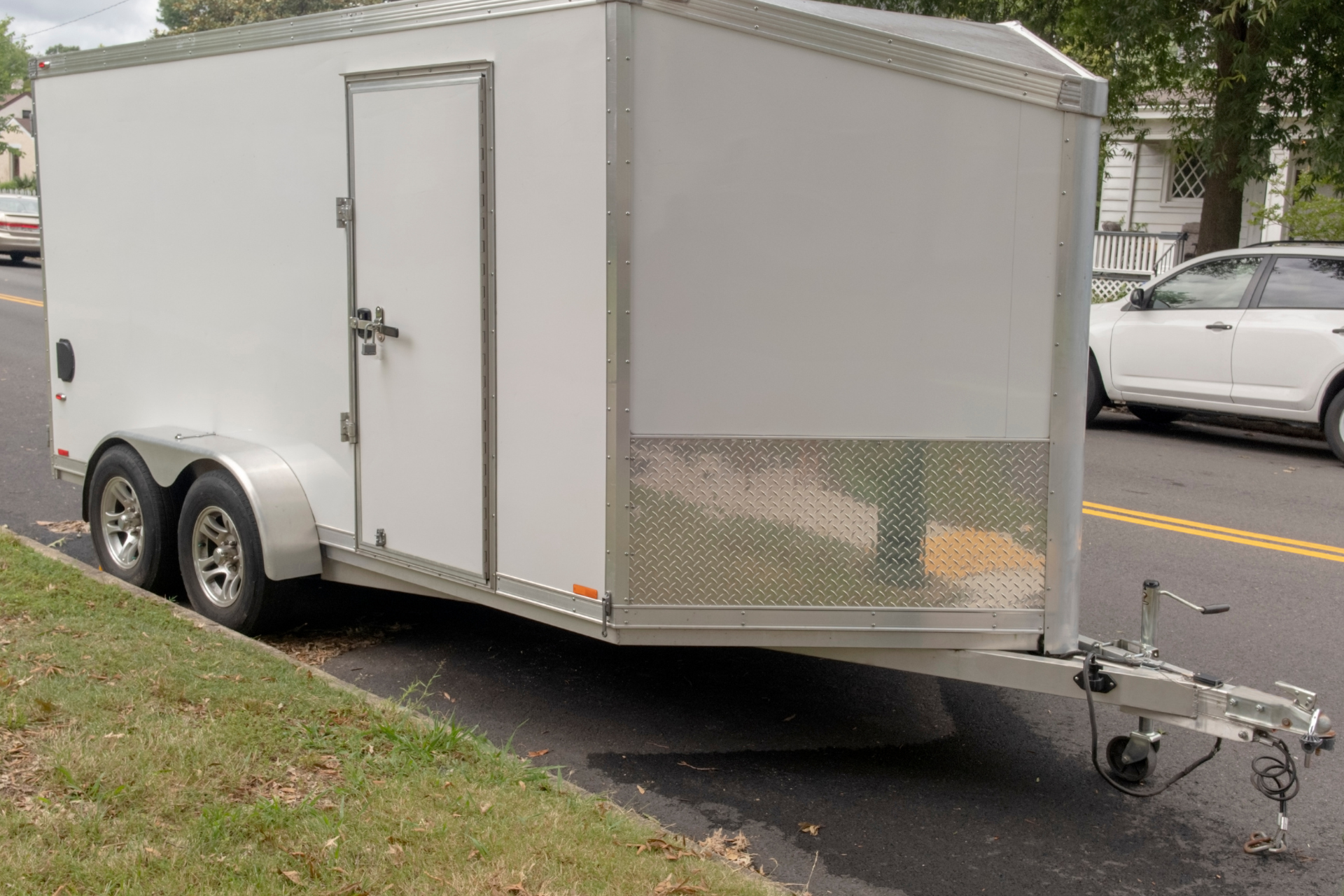 White enclosed cargo trailer parked on a street curb, with a hitch and dual axles.