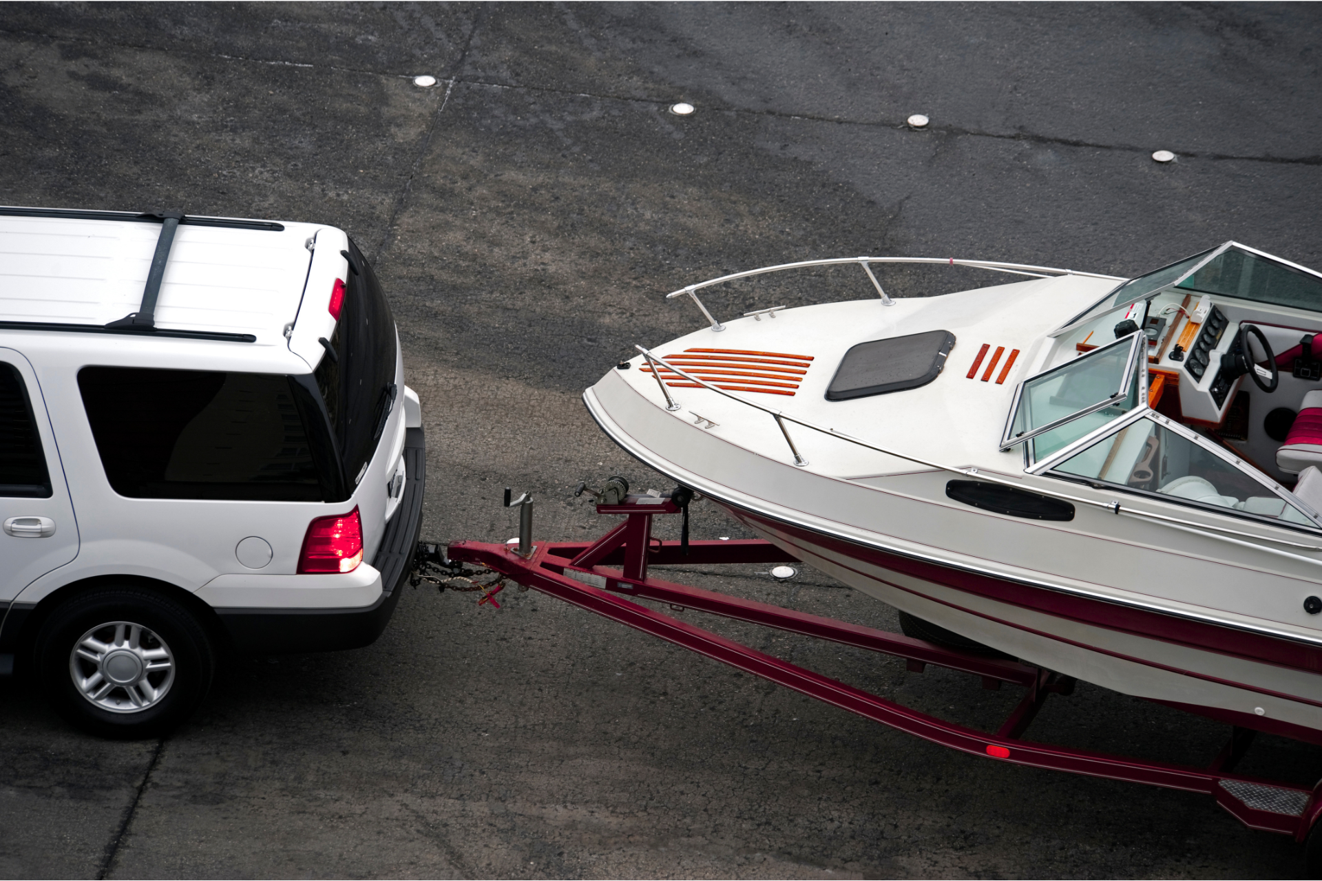 White SUV towing a white speedboat on a trailer in a parking lot