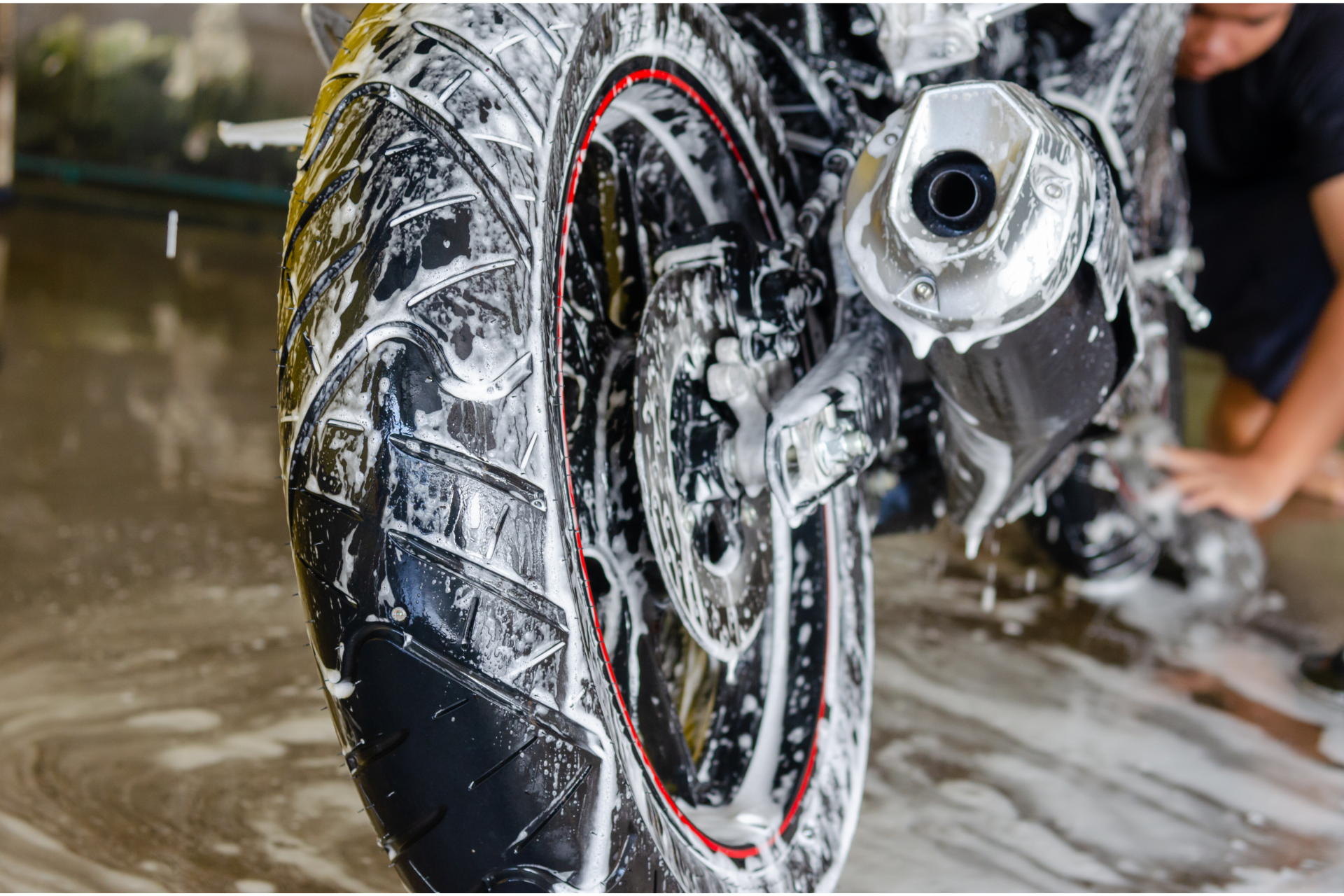 Close-up of a motorcycle wheel being washed with soap and water in a garage.
