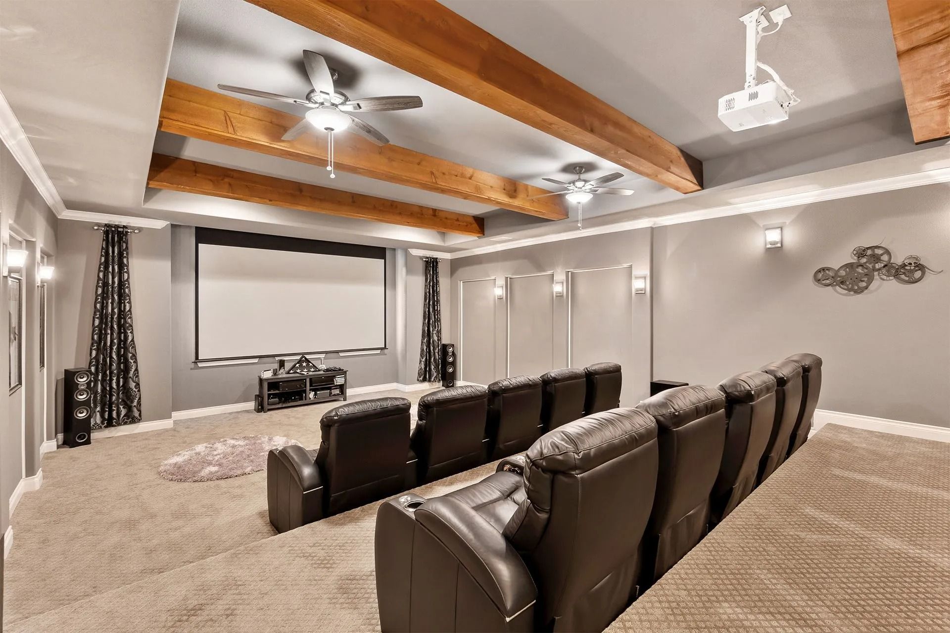 Spacious home theater with recliner seating, projector screen, and wood-beam ceiling fan.