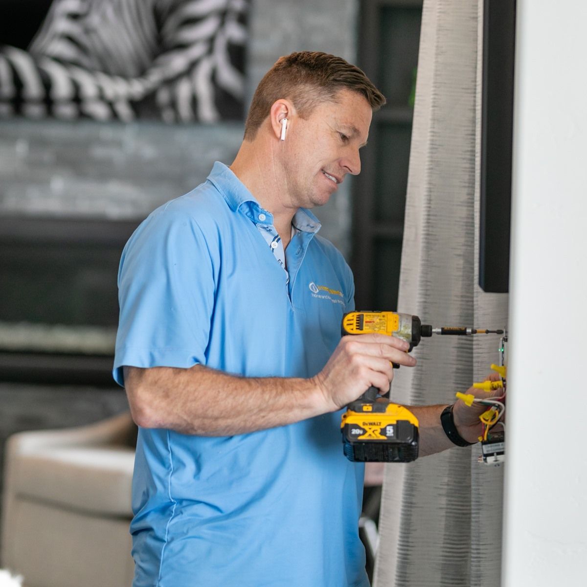 Technician in blue polo using a yellow drill to install a wall fixture indoors