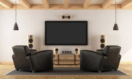 Modern home theater with large TV, surround speakers, and two black recliners on a rug