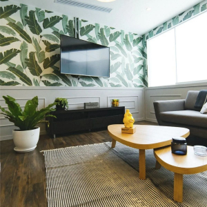 Modern living room with leaf wallpaper, wall-mounted TV, sofa, and low wooden coffee tables.