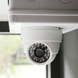 White security camera mounted under an overhang, angled downward indoors