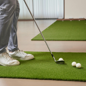 Golfer preparing to putt on indoor green turf beside two golf balls