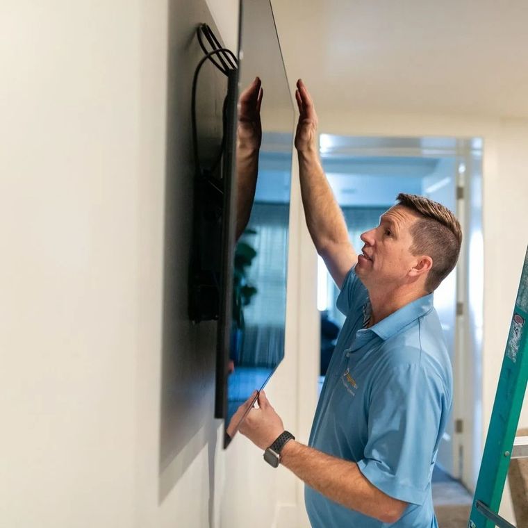 Technician mounting a flat-screen TV on a wall with a ladder nearby