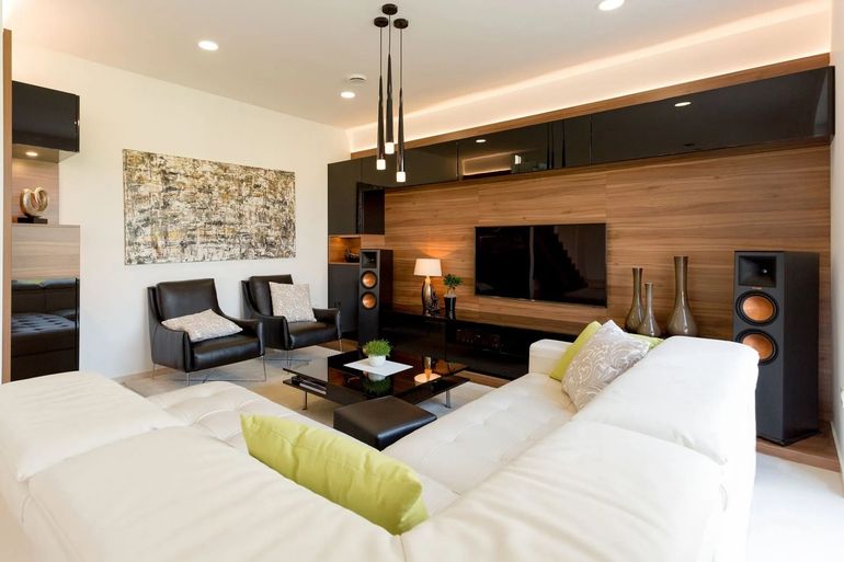 Modern living room with white sectional sofa, wood TV wall, black chairs, and warm recessed lighting
