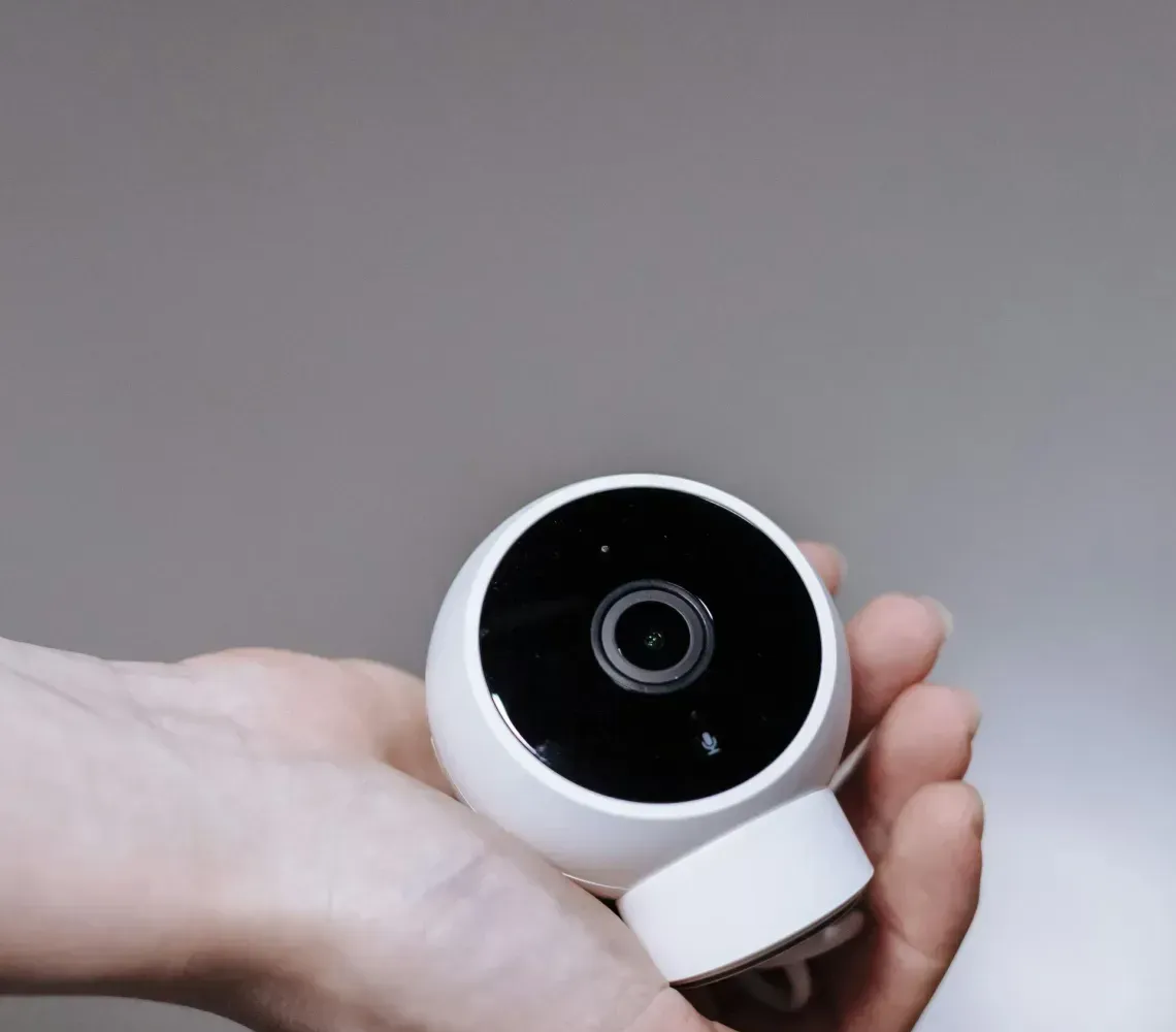 Hand holding a small white-and-black circular camera against a plain gray background