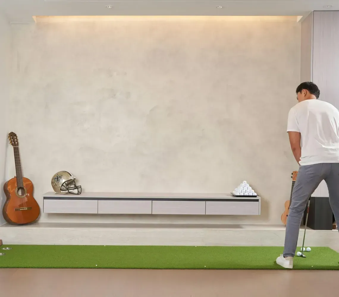 Man standing by a white wall in a minimalist room with a guitar, shelf, and green rug