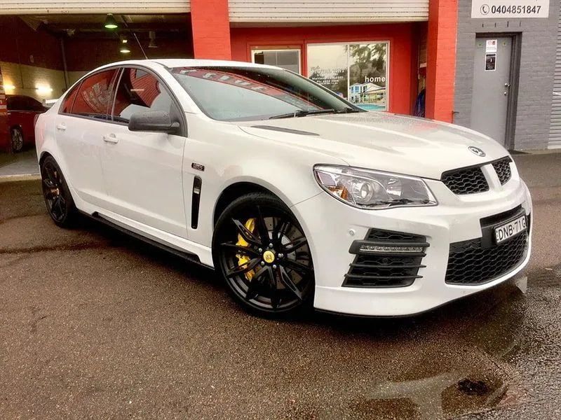 A White Car With Black Wheels is Parked in Front of a Building — Rod's Total Tint In Metford, NSW