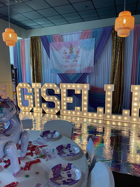 A room decorated for a birthday party with tables and chairs and a large lighted sign that says giselle.