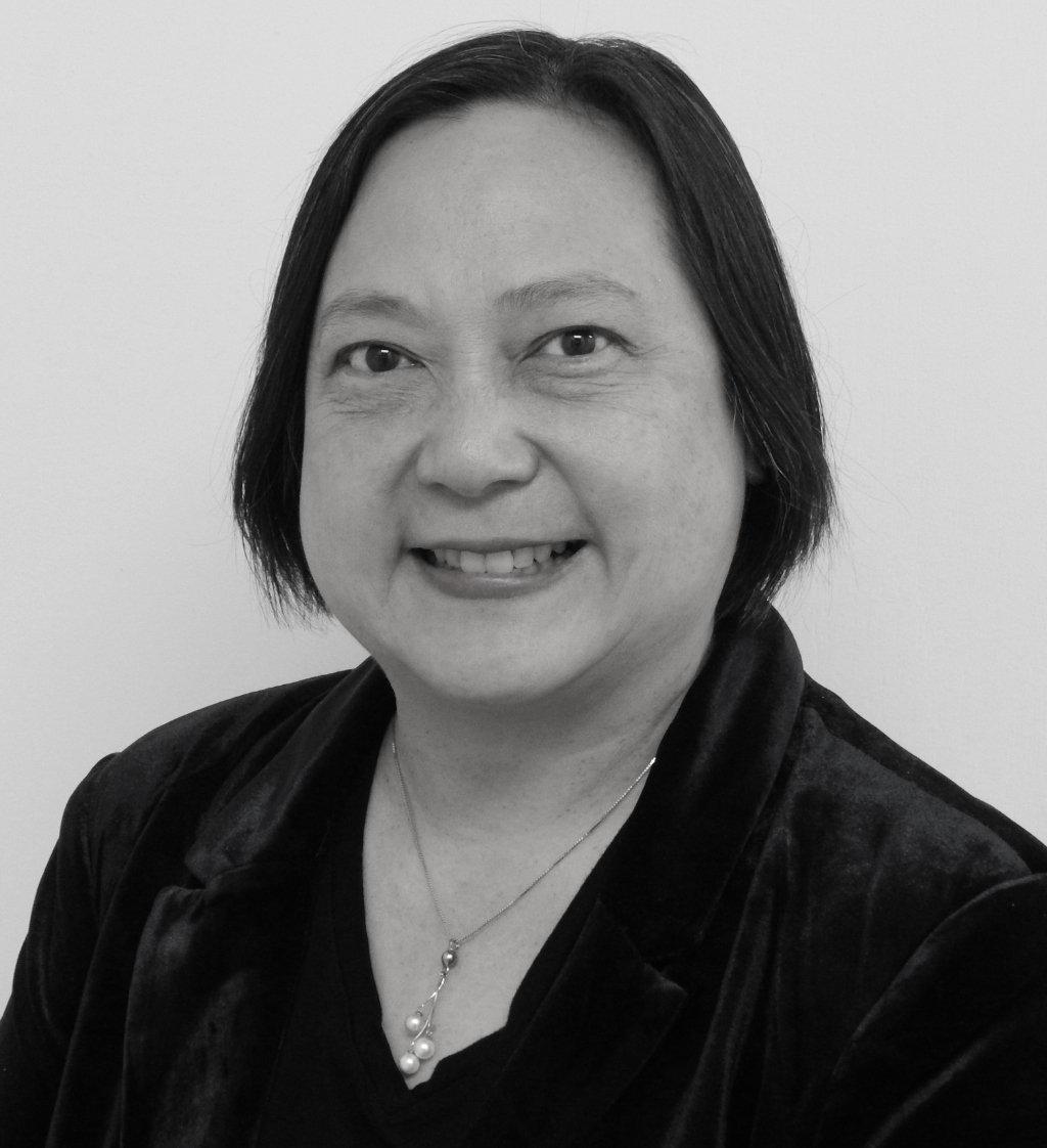 A woman wearing a black jacket and a necklace is smiling in a black and white photo.