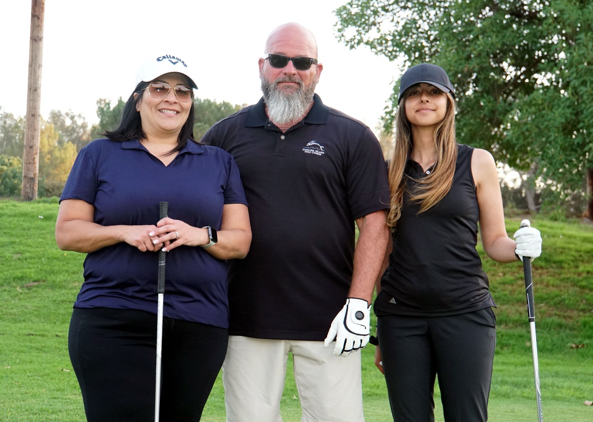 A man and two women are standing on a golf course holding golf clubs.