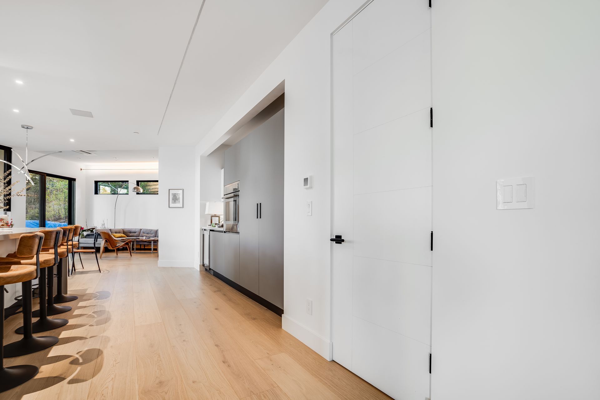 Bright modern kitchen and dining area with white walls, wood floors, and black chairs
