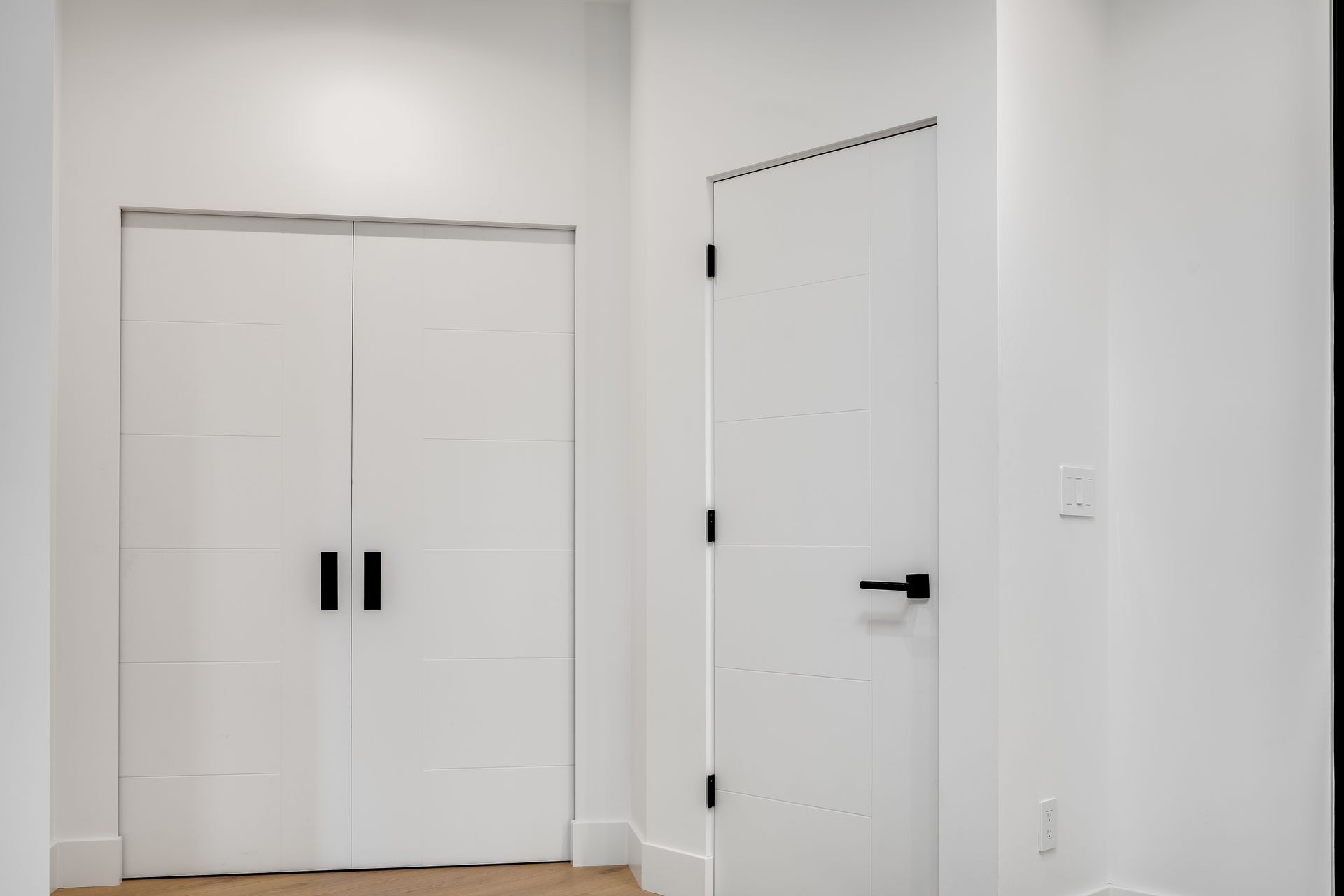 White hallway with double closet doors and a single white door with black handles and hinges