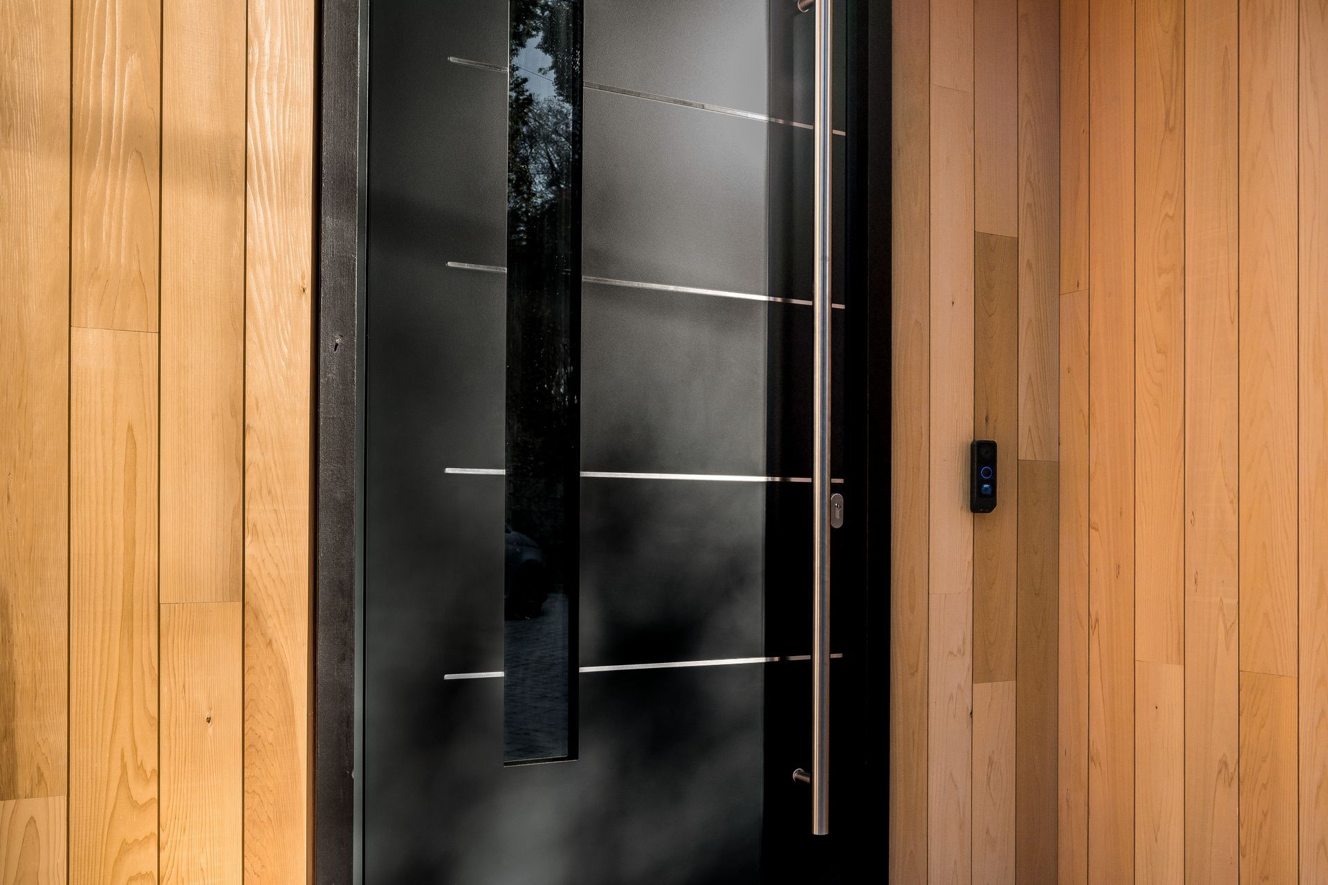 Modern black front door with vertical glass panels set in a wood-paneled wall